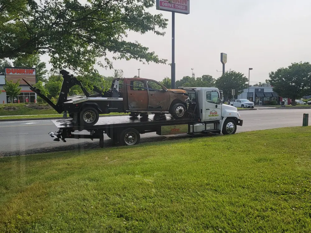 PRM flatbed tow truck carrying a fire-damaged crew cab pickup on its deck.